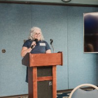 Susan Proctor holds microphone as she talks to GVSU Alumni with Leading the Way to D.C. graphic behind her